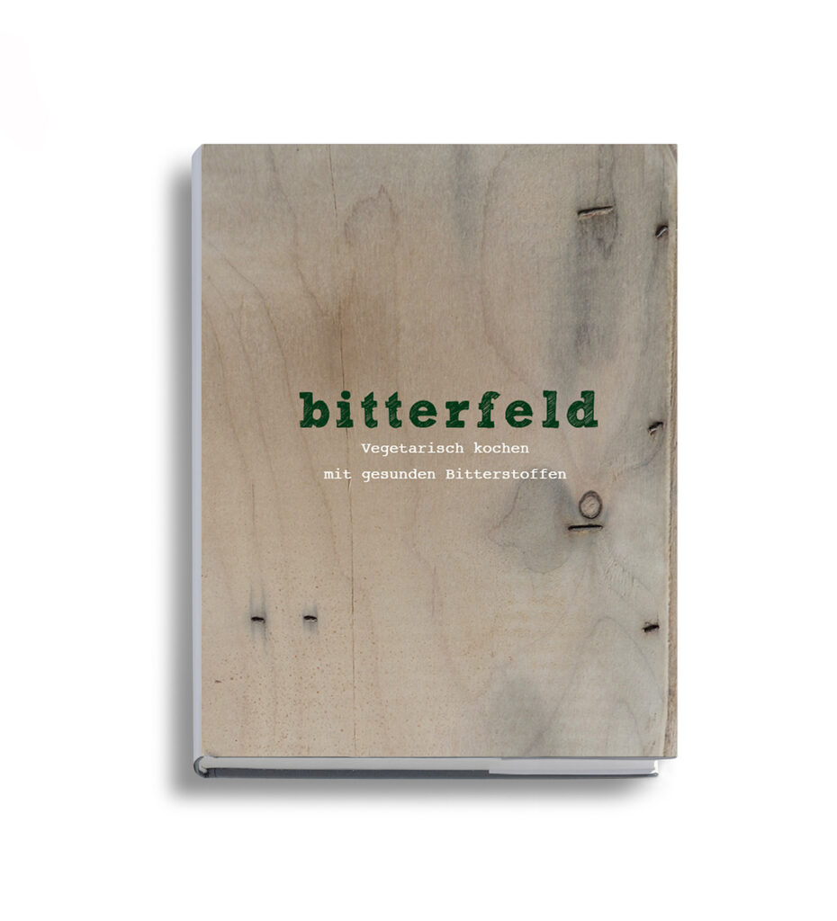 Mock Up des Kochbuches "Bitterfeld" Der Bucheinband ist wie eine Art Holzkiste gestaltet. Auf dem Titel steht in dunkelgrüner Typografie "Bitterfeld". Darunter, in kleiner, weißer Typografie, ist der Satz "Vegetarisch Kochen mit gesunden Bitterstoffen" zu lesen.